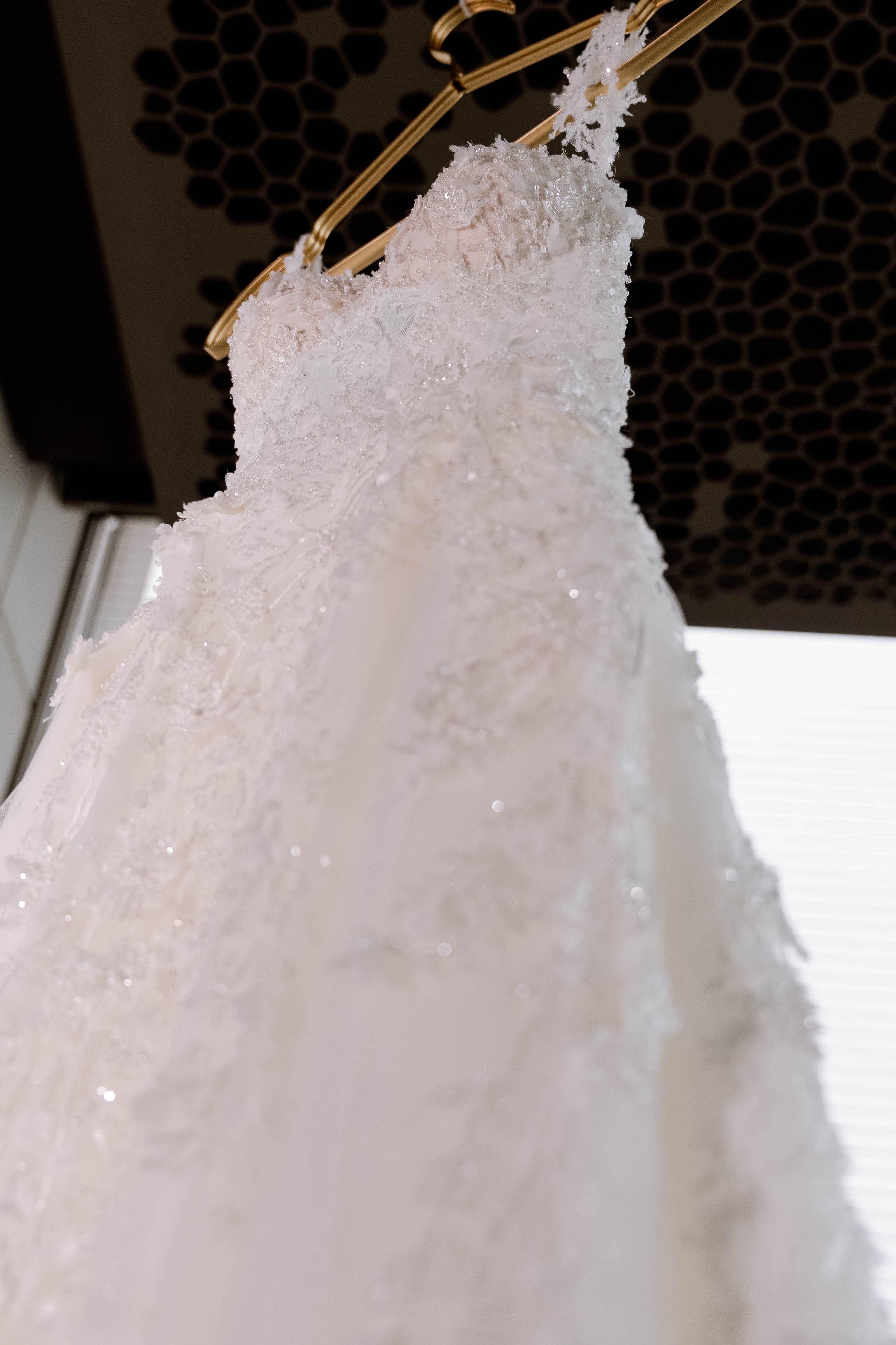 Brautkleid mit Spitze und Perlenstickerei am Bügel im Atelier
